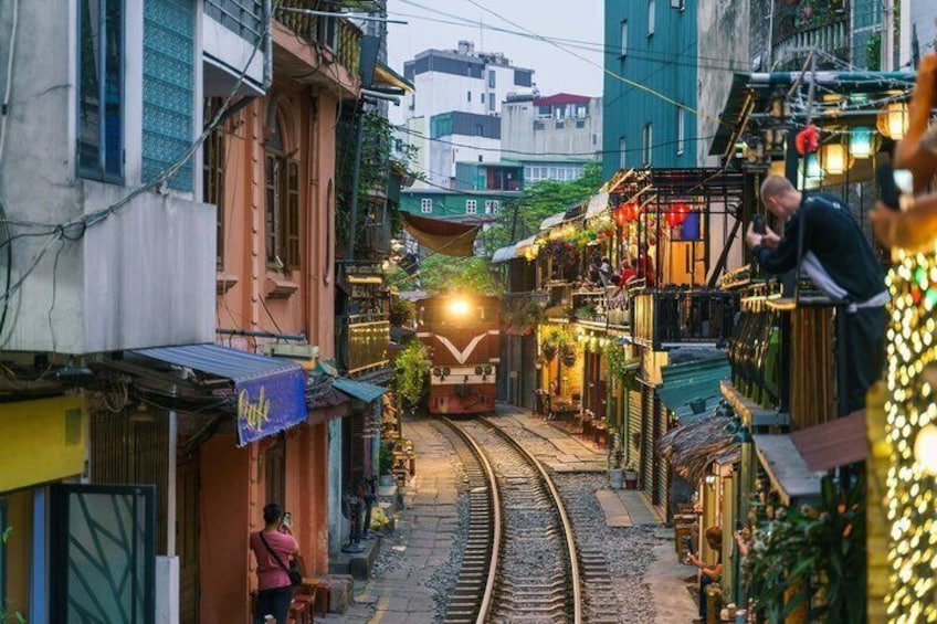 A narrow street with a train track, buildings, and a person standing by the track. 1