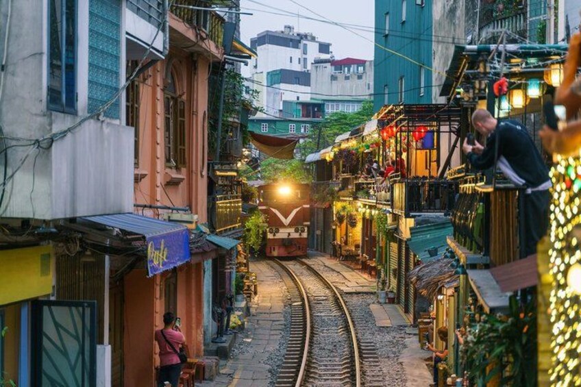 A narrow street with a train track, buildings, and a person standing by the track. 1