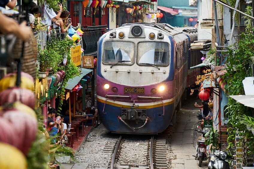 A train on tracks in a narrow street with buildings and people around. 5