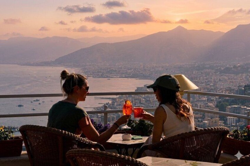 Two people sitting at a table with drinks, overlooking a city and mountains at sunset. 2