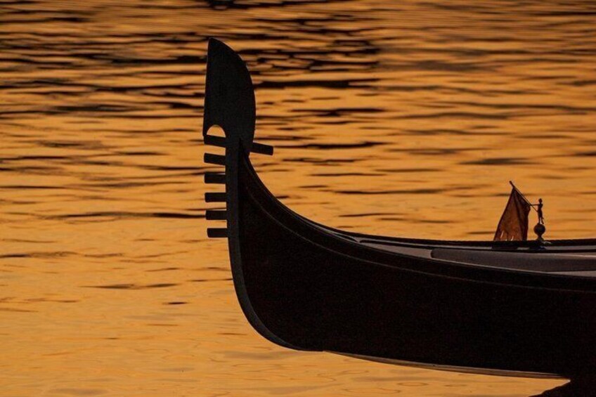 A traditional boat with a pointed bow and a small sail, floating on calm water during sunset. 1