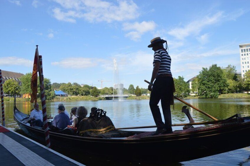 A gondola with a gondolier and passengers on a calm river, surrounded by trees and buildings. 2