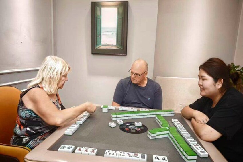 Three people playing mahjong at a table with tiles. 5