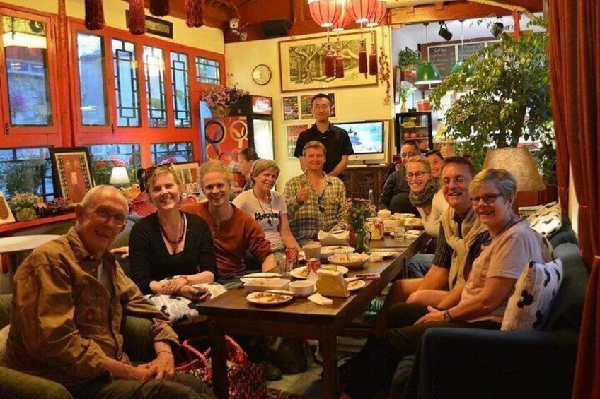 A group of people sitting around a table in a warmly lit room with red windows and various decorations. 1