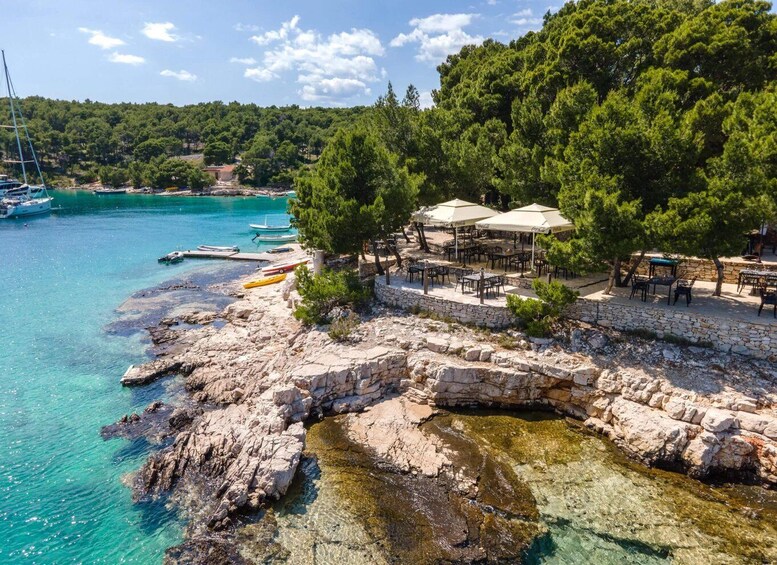 A coastal area with clear turquoise waters, rocky terrain, and a small outdoor seating area with umbrellas. 2