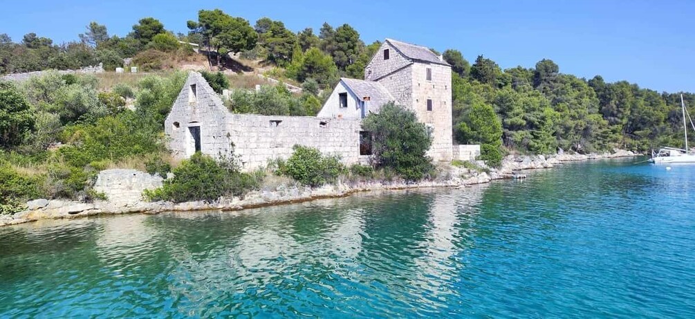 A coastal stone building with a tower, surrounded by clear blue waters and dense greenery. 3