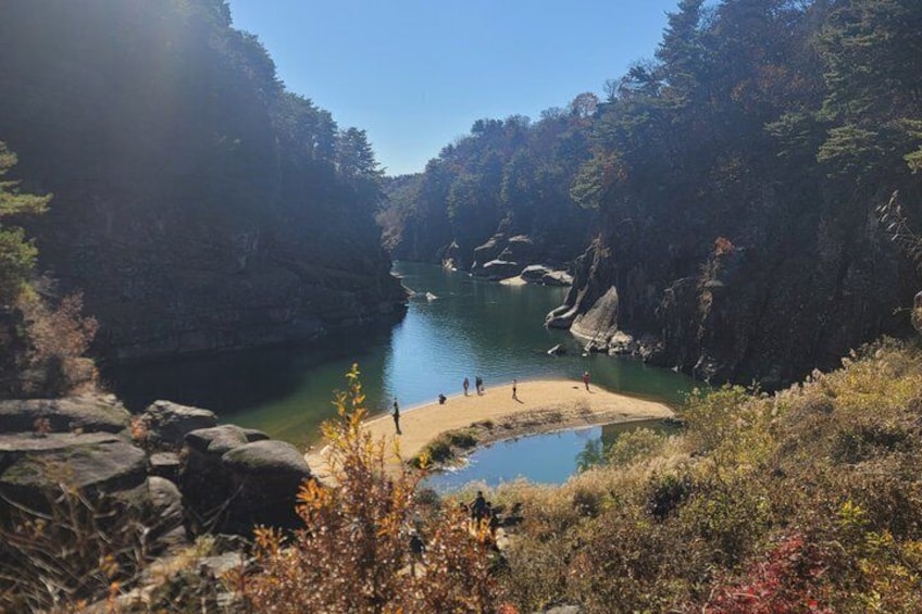 A river surrounded by cliffs, a sandy beach, and people walking. 3