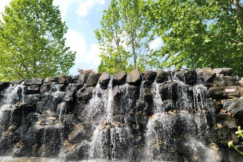A multi-tiered waterfall cascading over a rocky ledge, surrounded by lush green trees. 2