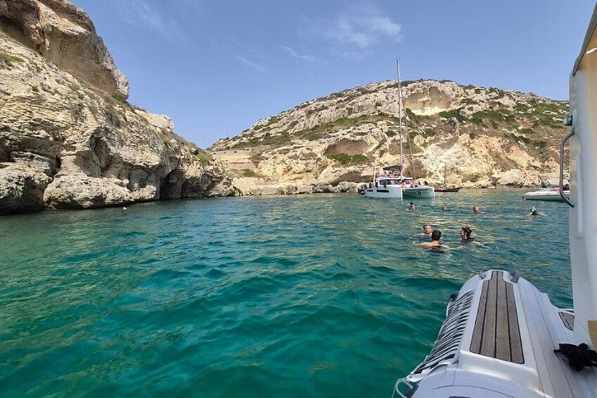 A boat on turquoise water, rocky cliffs, and a sailboat in the distance. 3