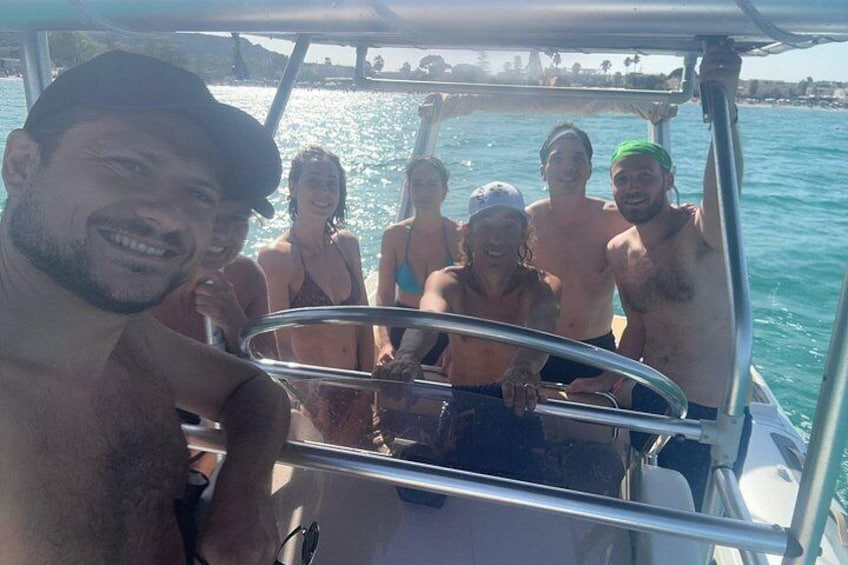 A group of people on a boat with a metal railing, water, and a distant shoreline. 4