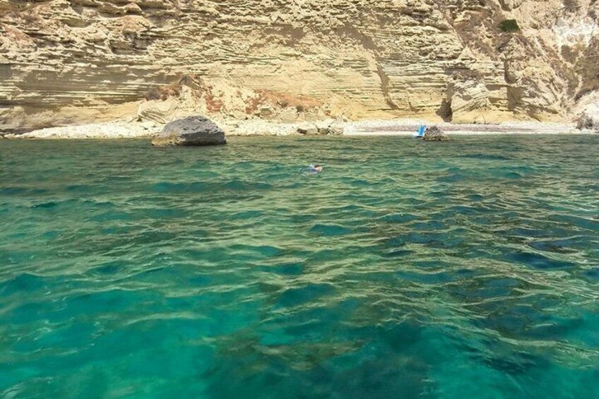 Clear turquoise water, a rocky shoreline, and a small blue object on the beach. 5