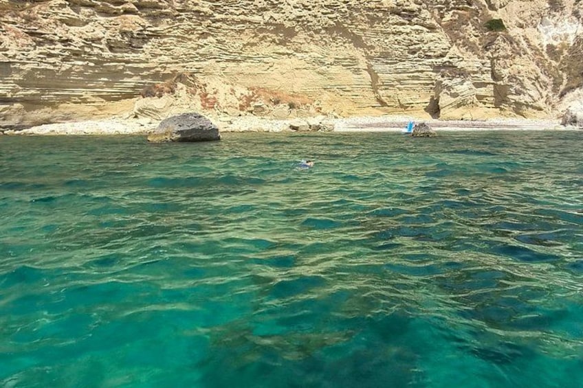 A clear blue sea, rocky cliffs, and a small boat. 2