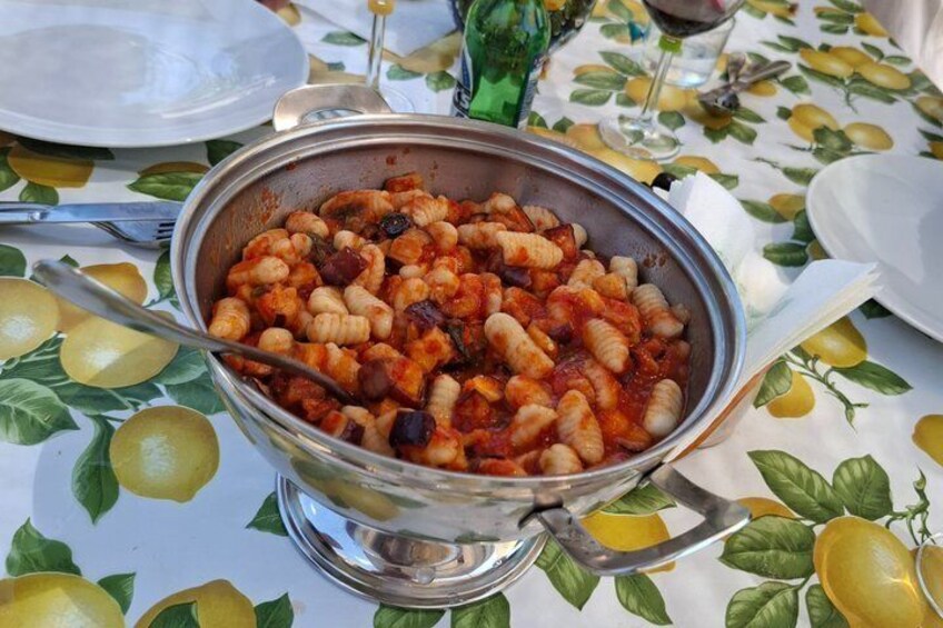 A bowl of pasta with a tomato-based sauce, placed on a table with a lemon pattern. 5