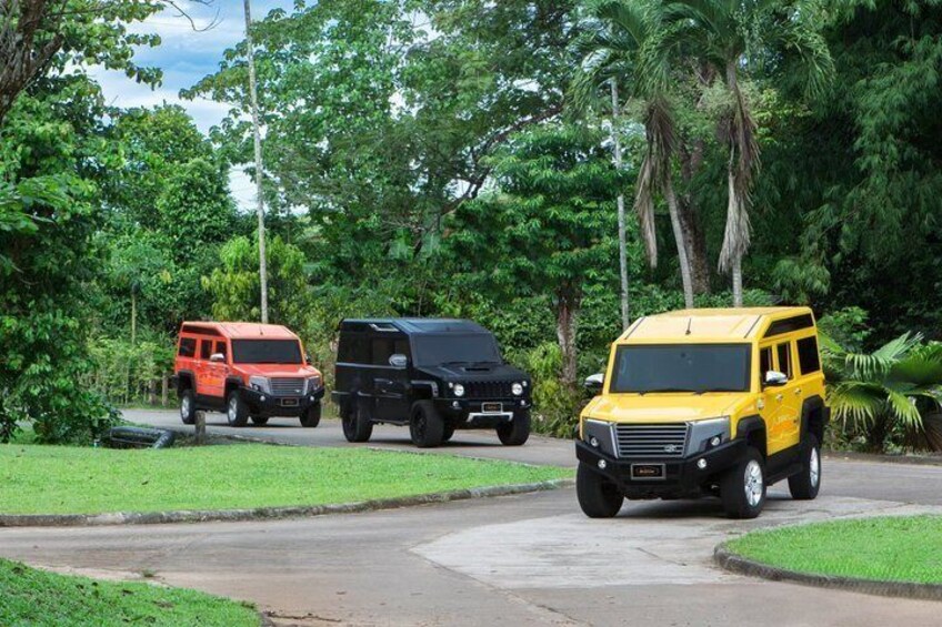 Three off-road vehicles on a paved road surrounded by lush greenery. 1