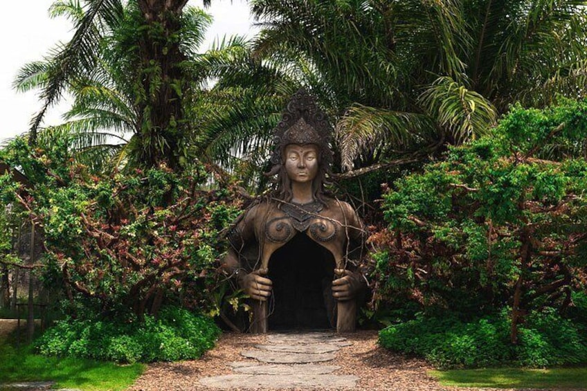 A statue of a woman with a headdress, standing in a tropical garden with palm trees and dense foliage. 2