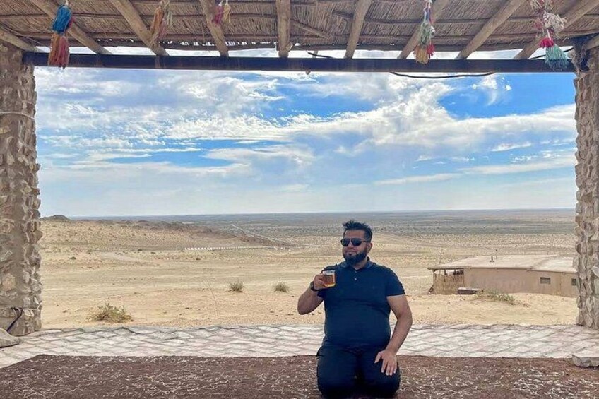 A person standing under a wooden structure with a desert landscape in the background. 2