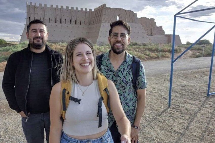 Three people standing in front of a large, ancient structure with a desert landscape in the background. 1