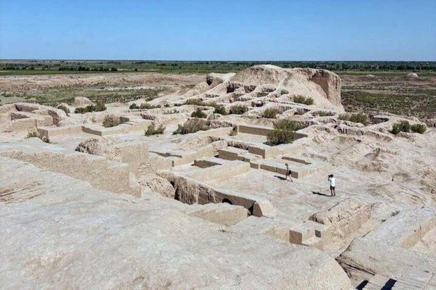 Ancient ruins with stepped structures and a large mound in a desert landscape. 2