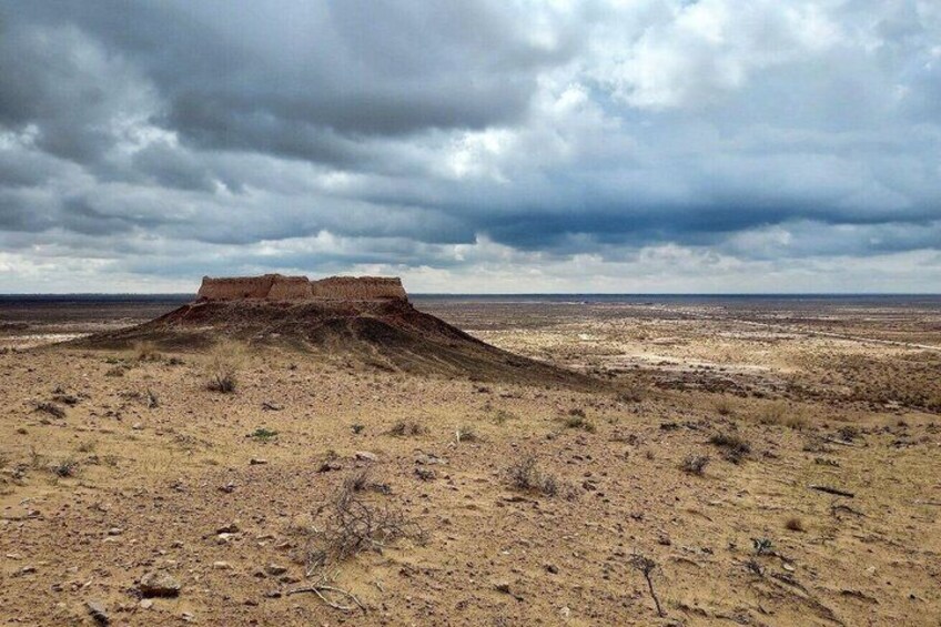 A barren landscape with a prominent hill and a flat horizon under a cloudy sky. 4