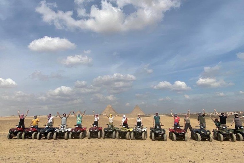 A group of people on ATVs in a desert with pyramids in the background. 1