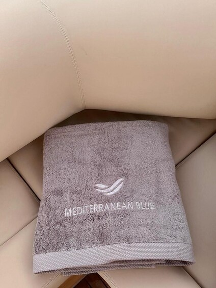 A folded towel with 'Mediterranean Blue' text and a logo on a beige couch. 5