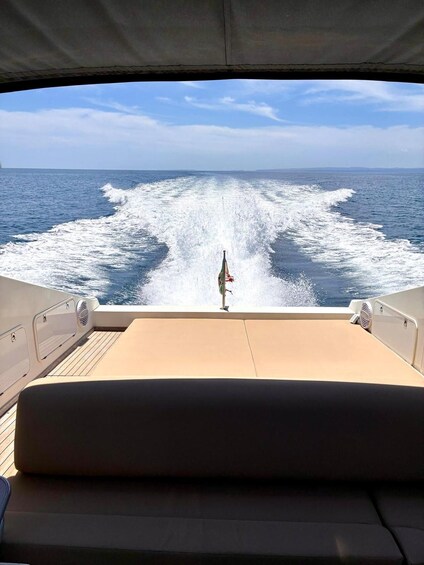 A boat's deck with a wake in the ocean, a flag, and a clear sky. 4