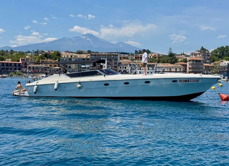 A white boat named '1ROMA33410' on calm water with a mountainous backdrop. 1