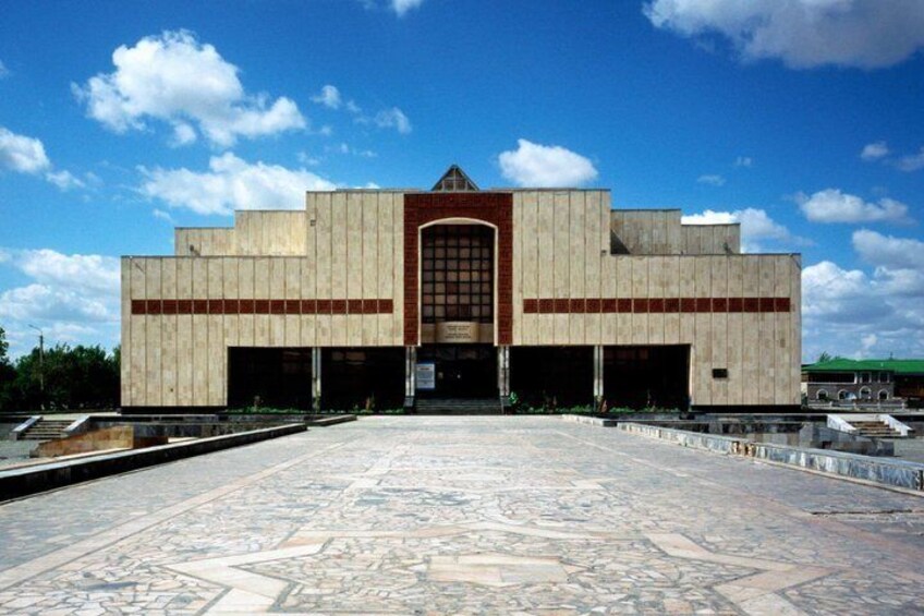 A large building with a symmetrical facade, a central entrance, and a patterned floor in front. 1