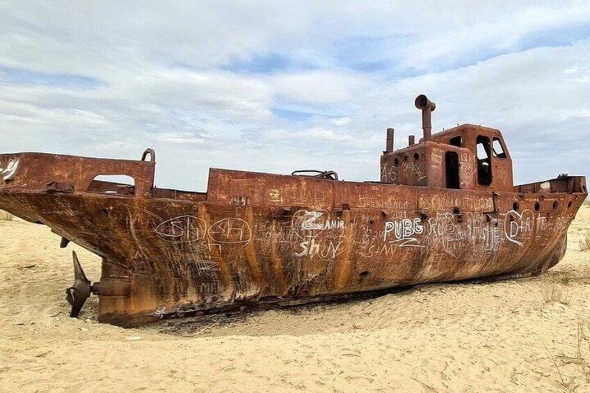 A rusted shipwreck on a sandy beach with graffiti. 2