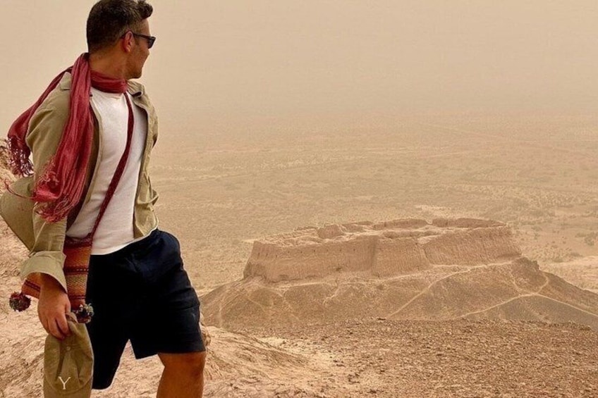 A person standing on a sandy terrain overlooking ancient ruins. 1