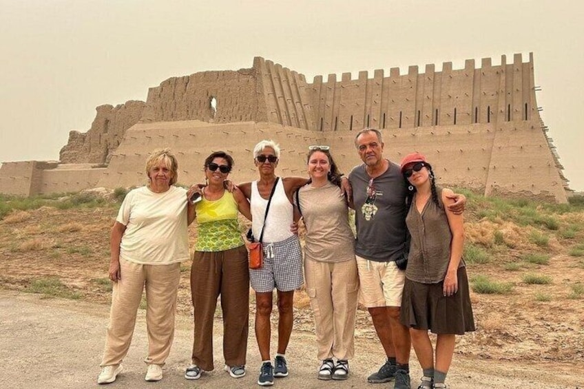 A group of people standing in front of an ancient fort-like structure. 1