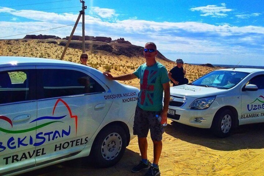 A desert landscape with two cars parked on the sand. 1