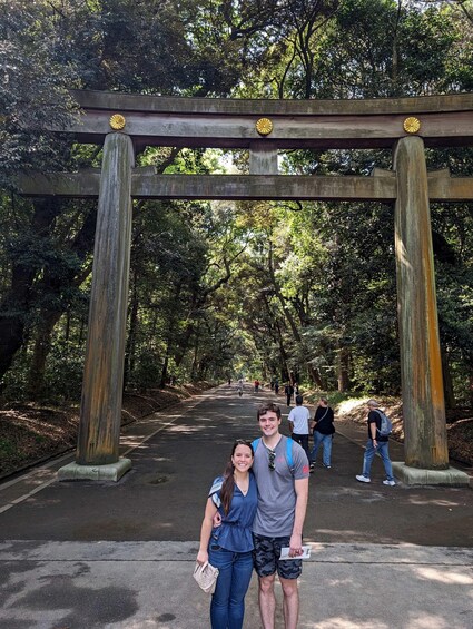 A couple standing under a traditional Japanese torii gate in a forested area with a pathway. 4