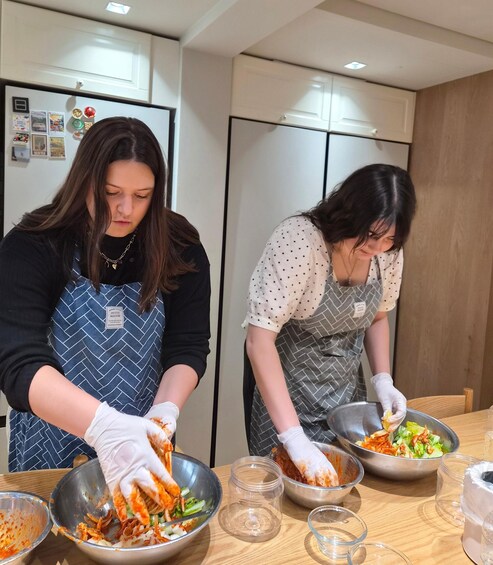 Two individuals preparing food in a kitchen, wearing aprons and gloves. 2