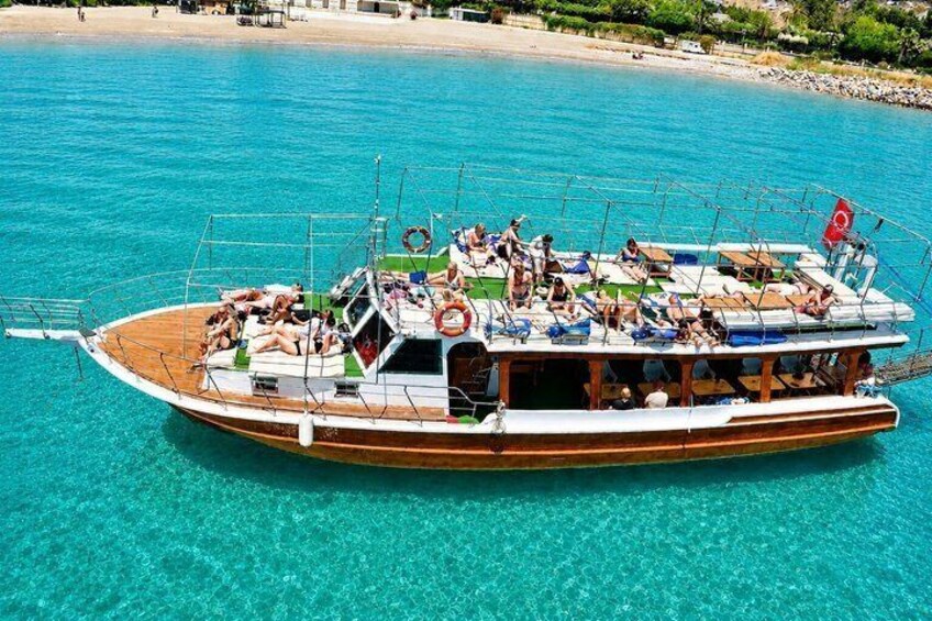A wooden boat with passengers on a clear turquoise sea, near a sandy beach. 1