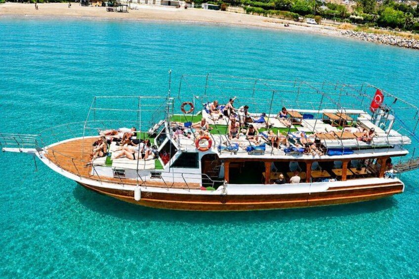 A wooden boat with passengers on a clear blue sea, near a sandy beach. 1