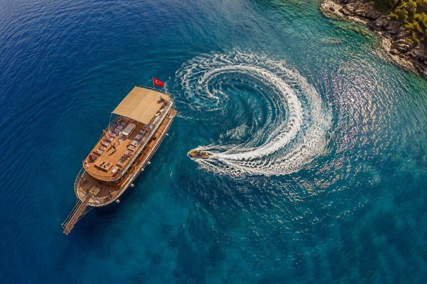 A boat creating a wake in clear blue water, with a rocky coastline in the background. 5