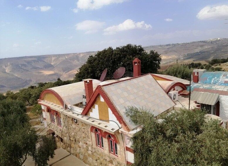 A stone building with red accents and a satellite dish, surrounded by trees and a mountainous landscape. 5