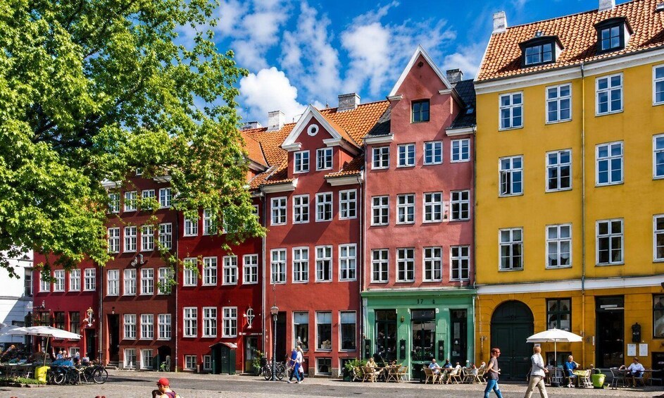 Colorful buildings with red, pink, green, and yellow facades, a cobblestone street, and outdoor seating areas. 3