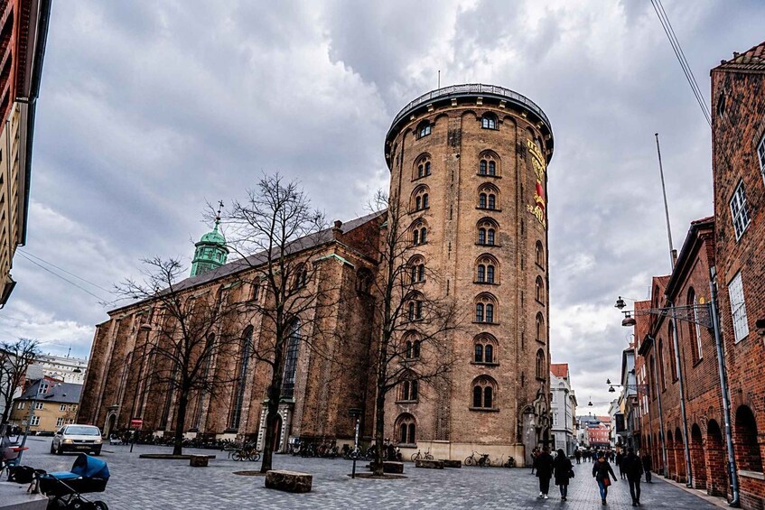 A historic building with a round tower, a green dome, and a cobblestone square. 2