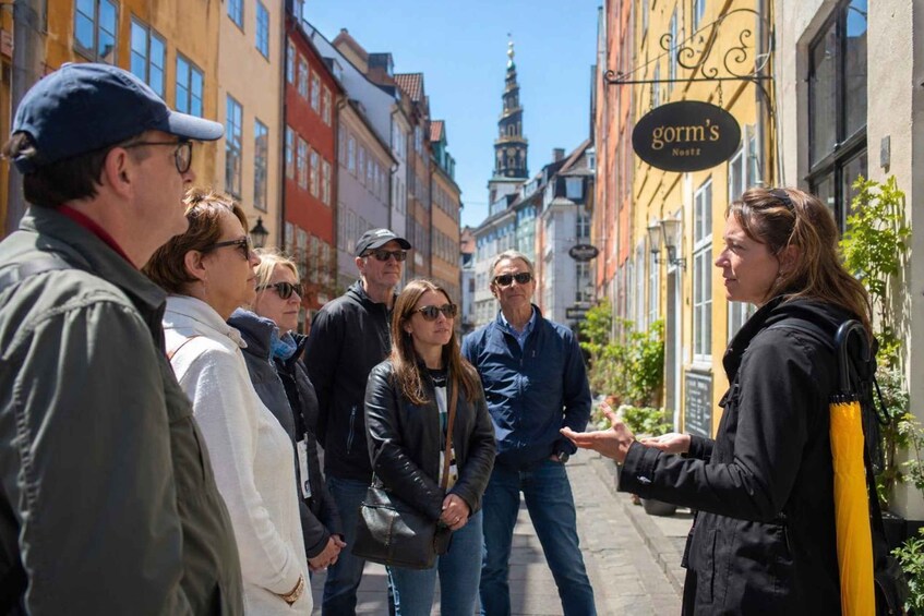 A group of people standing on a street, a building with a sign that reads 'gorm's Nostr', and a tower in the background. 1