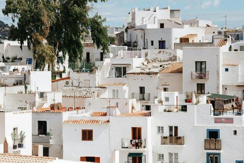 A densely packed urban area with white buildings, some with balconies, and a large tree in the foreground. 4