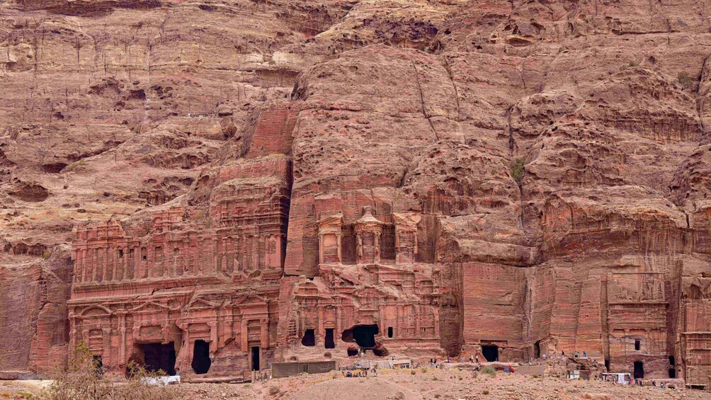 Ancient rock-cut architecture with multiple levels and niches, set against a rugged, reddish-brown cliff. 3