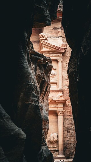 A carved rock facade with columns and a central relief, framed by natural rock formations. 1