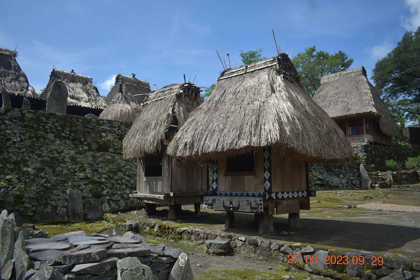 Traditional thatched-roof huts with wooden walls, set against a backdrop of stone walls and a clear sky. 4