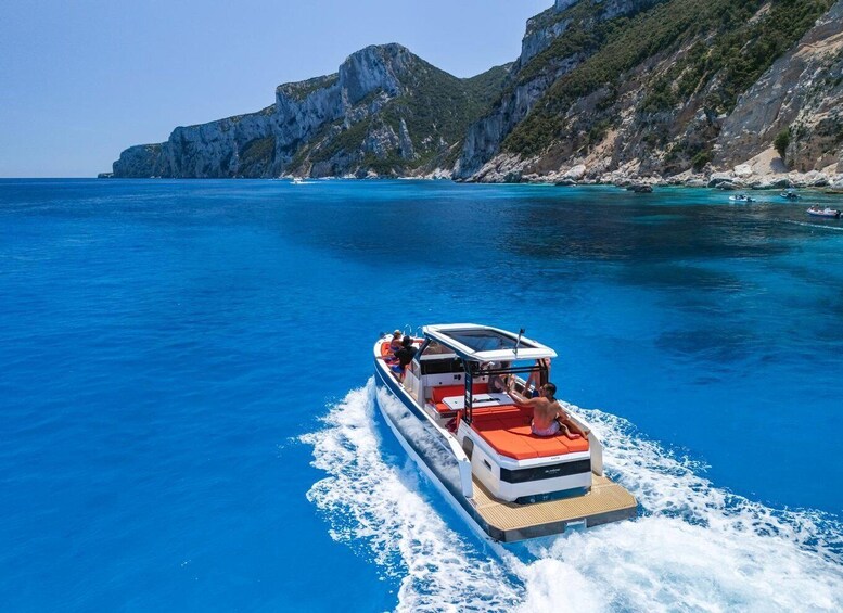 A boat with passengers on a clear blue sea with rocky cliffs in the background. 3