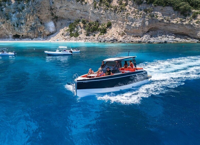 A boat with passengers on a clear blue sea, surrounded by rocky cliffs and other boats. 1