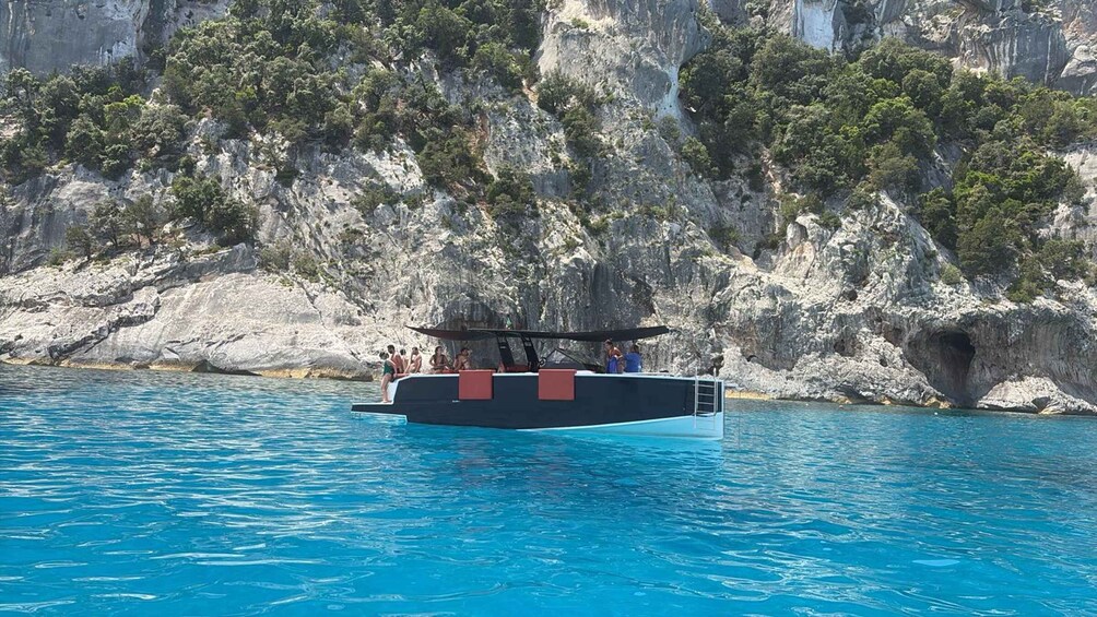 A boat with people on a clear blue sea, surrounded by rocky cliffs. 2