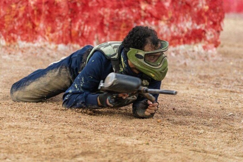 A person lying prone on the ground aiming a rifle, with a red target in the background. 4