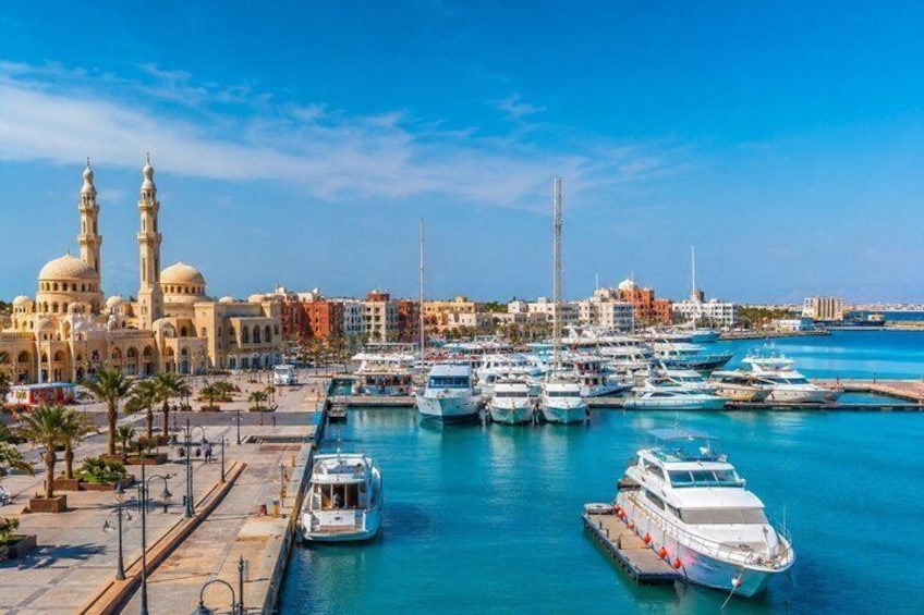 A marina with boats docked, a mosque with two minarets, and a clear blue sky. 1